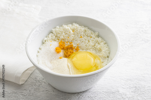 Ingredients for ricotta cheese filling in white bowl with raw egg orange zest semolina and sugar on kitchen table