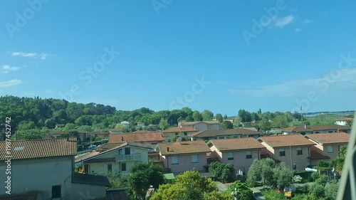 Countryside view from a moving train window with farmland, village houses, green fields and clear blue sky. Scenic travel footage with peaceful suburban panorama.