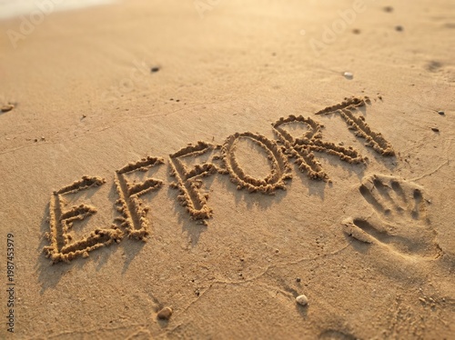 Word effort written in sand on beach with handprint next to it on sunny day
