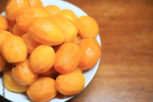 Fresh peeled Thai marian plums, also known as mayongchid or maprang, arranged in a white bowl on a wooden table. 
