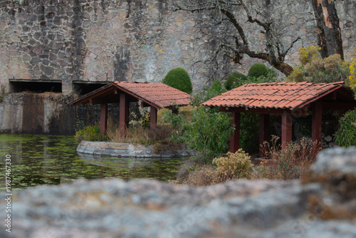 Wooden pavilions with red tile roofs next to a pond with aquatic vegetation