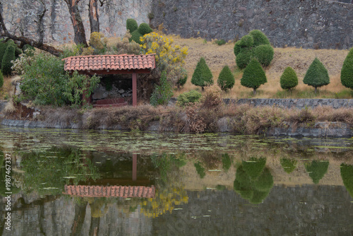 Small shelter with a red tiled roof next to a pond