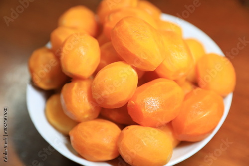 Fresh peeled Thai marian plums, also known as mayongchid or maprang, arranged in a white bowl on a wooden table. 
