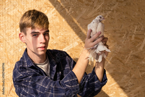 A young man in a plaid shirt proudly shows off his beautiful white pigeon