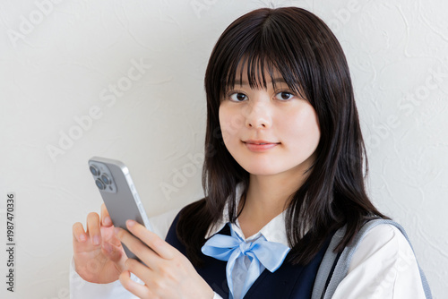 スマートフォンを操作する女子高校生のポートレート（白背景・通学シーン）
