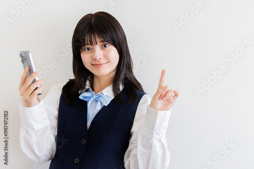 スマホを持ち指差しでアイデアを示す女子高校生（白背景・コピースペース）
