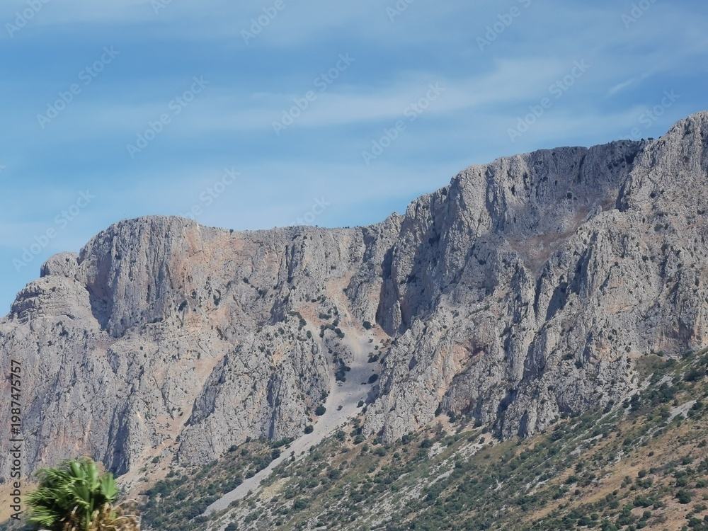 Fototapeta premium Majestic rocky cliffs of Sicilian landscape under a clear blue sky, showcasing the natural beauty of Sicily, Italy with lush greenery at the base