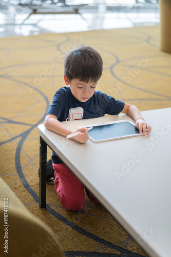 Young Boy Engaged with Tablet at Airport Lounge, Focused and Curious