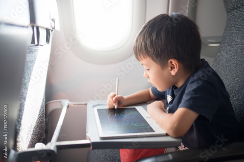 5 Year Old Boy Engaged in Creative Drawing on a Tablet While Traveling in an Airplane