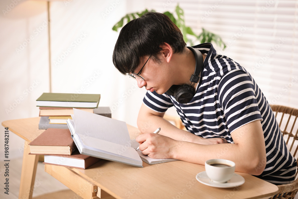 Fototapeta premium Student in glasses with headphones preparing for exam at wooden desk indoors