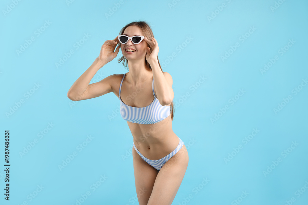 Obraz premium Beautiful woman wearing stylish swimsuit and sunglasses on light blue background