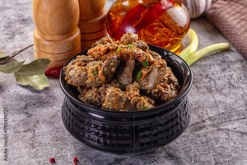 Billede på lærred Hearty stewed chicken liver with herbs and spices in a black bowl on a gray table