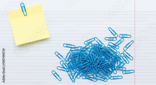 A pile of blue paper clips on a lined notebook page with a yellow sticky note