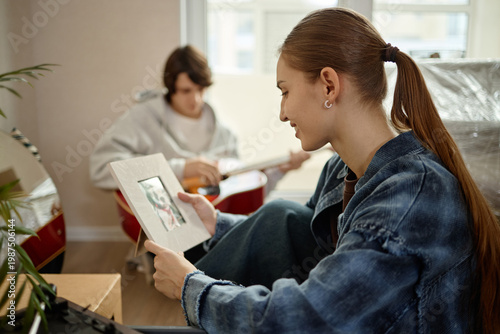 Schilderij op canvas Woman holding printed photo while moving into new home, man playing guitar in background