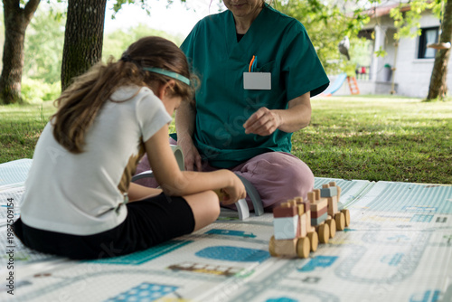 Quadro em tela A healthcare worker in green uniform sits with a child on a play mat, facilitating an early intervention session focused on stimulation and growth