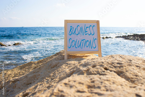 Business Solutions symbol. Blackboard with Concept words Business Solutions. Beautiful sea background. Business and Business Solutions concept. Copy space.