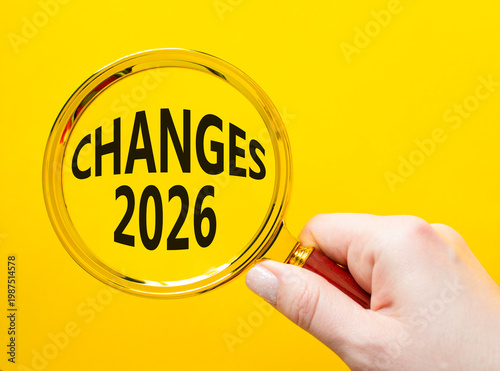 Changes 2026 symbol. Magnifying Glass with words Changes 2026. Beautiful yellow background. Businessman hand. Business and Changes 2026 concept. Copy space.