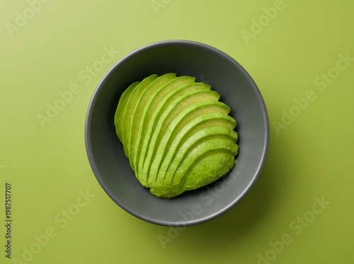 Top view of fresh sliced green avocado in a dark bowl on a green background