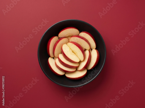 Top view of fresh sliced red apple in a dark bowl on a red background