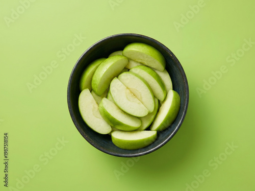 Top view of fresh sliced green apple in a dark bowl on a green background