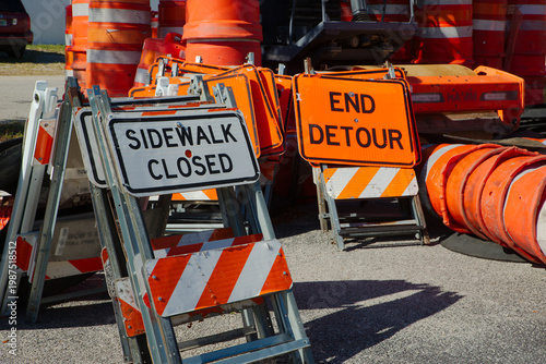 Vászonkép Bright orange End Detour signs and stacked traffic cones rest on pavement at a road construction site, conveying traffic control, temporary closure, and urban maintenance work in daylight