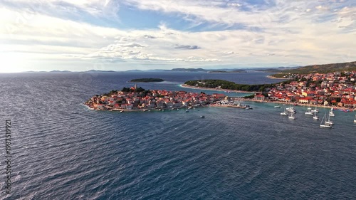 Aerial view of Primosten old town on the Adriatic coast in Croatia, featuring red-roofed houses, blue sea, and boats in the harbor
