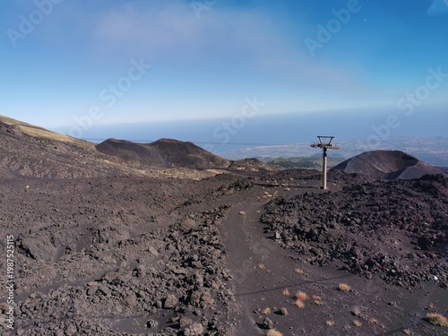 Mount Etna landscape featuring volcanic terrain, rocky paths, and a ski lift against a clear blue sky in Sicily, Italy, showcasing the natural beauty of an active stratovolcano