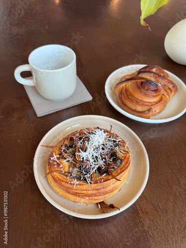 Morning coffee served with fresh cinnamon rolls and pastries.

A high-angle shot of a breakfast table featuring an empty white coffee mug on a coaster, paired with two different types of 