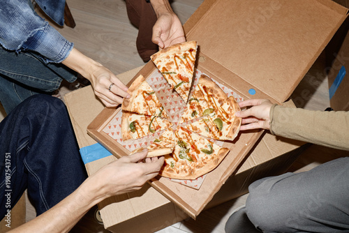 Foto Overhead shot of young adults sharing pizza from delivery box, grabbing slices during casual group meal