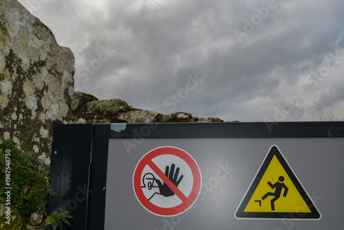 Industrial safety signage on a gray fence wall, including a no entry symbol and a falling hazard warning. Concept of danger, security, and workplace caution.