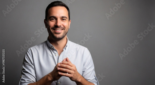 Smiling man with hands clasped in front of him against a plain gray background