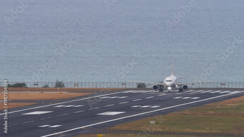 Footage of a passenger jet airplane preparing for takeoff on coastal runway with the ocean in the background. The aircraft lines up on the centerline, ready for departure against a scenic seaside view