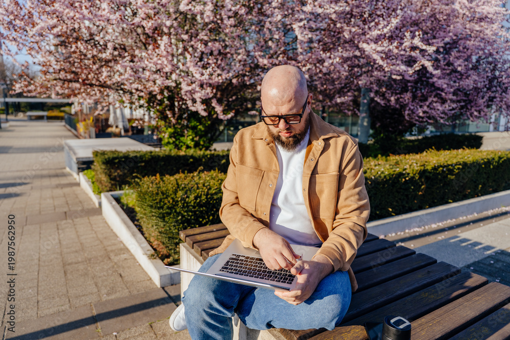 Fototapeta premium White man checking time while working on laptop outdoors spring multitasking