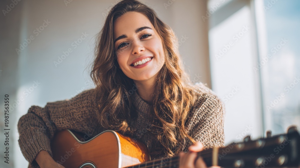 Fototapeta premium Young woman plays acoustic guitar in bright music room with warm background and casual outfit