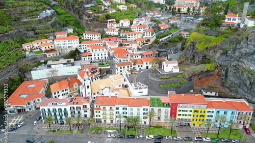 Aerial view of Ponta do Sol, Madeira, showcasing its vibrant coastal architecture, terraced hills, and pebble beach under a clear afternoon sky. A picturesque island escape.