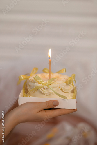 Caucasian Hand Holding Lit Cake With Candle, Delicate Yellow Ribbon And Buttercream In Small Box Soft Warm Lighting, Closeup On Manicured Fingers Suggesting Intimate Wish And Quiet