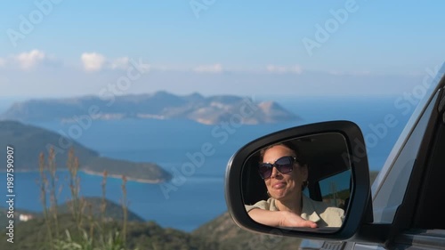 Woman driving car enjoying coastal road trip. Beautiful woman with sunglasses reflecting in a car's side mirror during a scenic road trip with a stunning coastal landscape in the background