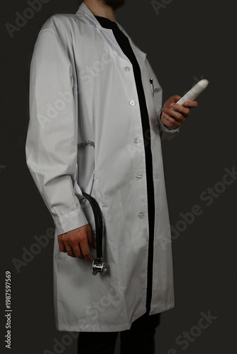 A standing doctor is holding a telephone in one hand while a stethoscope is sticking out of the pocket of his doctor's coat 