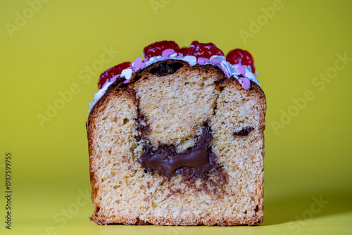 Sliced Easter sweet cake with chocolate filling and cherries on yellow background. Cross section of a sweet bread with melted chocolate inside decorated with icing sprinkles and cherries, closeup