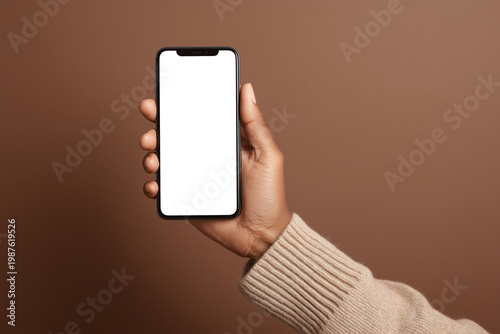 Person holding smartphone with blank black screen mockup on brown background, mobile app concept
