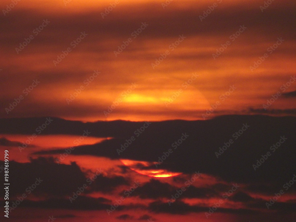 Obraz premium Dark dramatic sunset with sun hidden behind clouds intense sky background