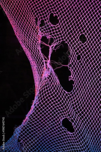 Vibrant pink and blue netting with holes against a dark background