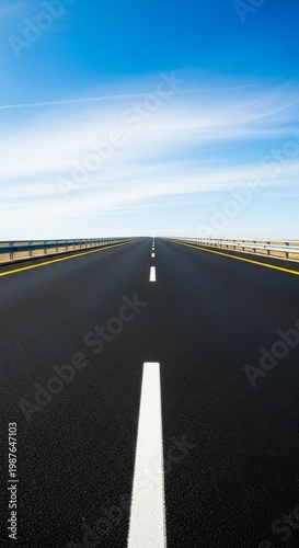 A clean asphalt highway stretches toward the horizon under a clear blue sky, featuring crisp white lane markings and yellow safety lines, path, motorway, transit