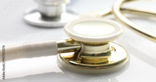 Two medical stethoscopes on white table, closeup. Camera moving right