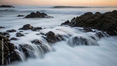 A long-exposure seascape of misty water flowing around coastal rocks.