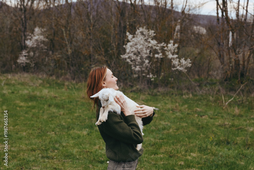 Tableau sur toile A woman outdoors in a green field holds a small goat kid close, smiling softly