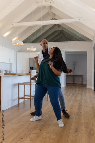 African American couple dancing together in open-plan kitchen near wooden island and pendant lights