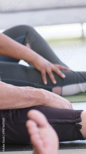 Vertical video: Turning coach in blue top guiding group legs and feet stretching at home with mats