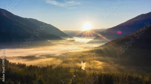 Golden sunrise illuminates misty valley with winding river and evergreen forest below mountain slopes.