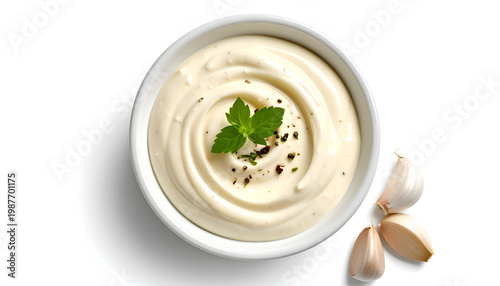 Creamy aioli sauce swirls in a white bowl with a sprig of fresh mint and garlic cloves on a white background for flavor and garnish